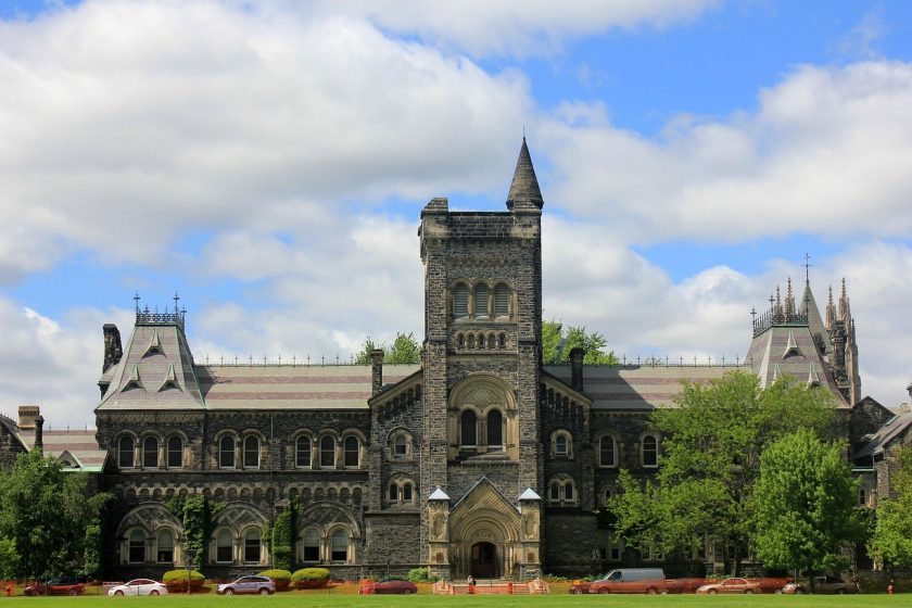 郑州大学主校区秋日校园风光，金黄银杏大道延伸至现代化图书馆，阳光温暖洒落，学生三三两两漫步其中，充满浓厚学术氛围